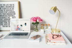 A white desk with a laptop, lamp, and flowers