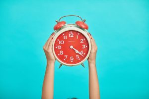 Hands holding analog clock against turquoise background