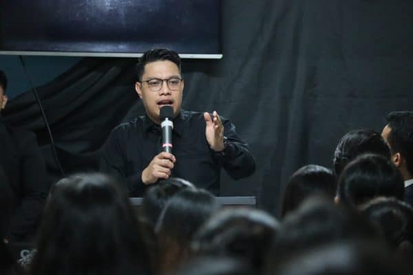 Man speaking to audience with microphone.