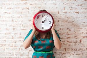 Lady holding clock in front of her face.