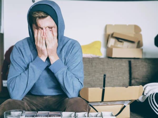 Person in blue hoodie with hands over face in frustration.