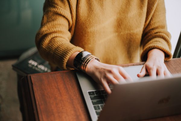 Lady in tan sweater typing on laptop.