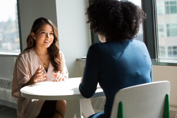 Two career women chatting on a white table.